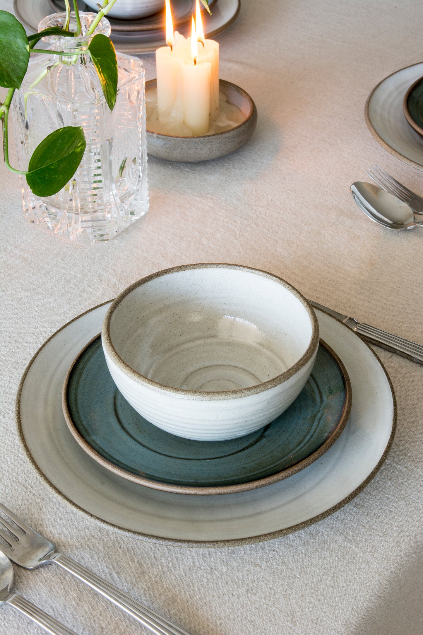 Elegant table setting with ceramic bowls, plates, and candles on a neutral background