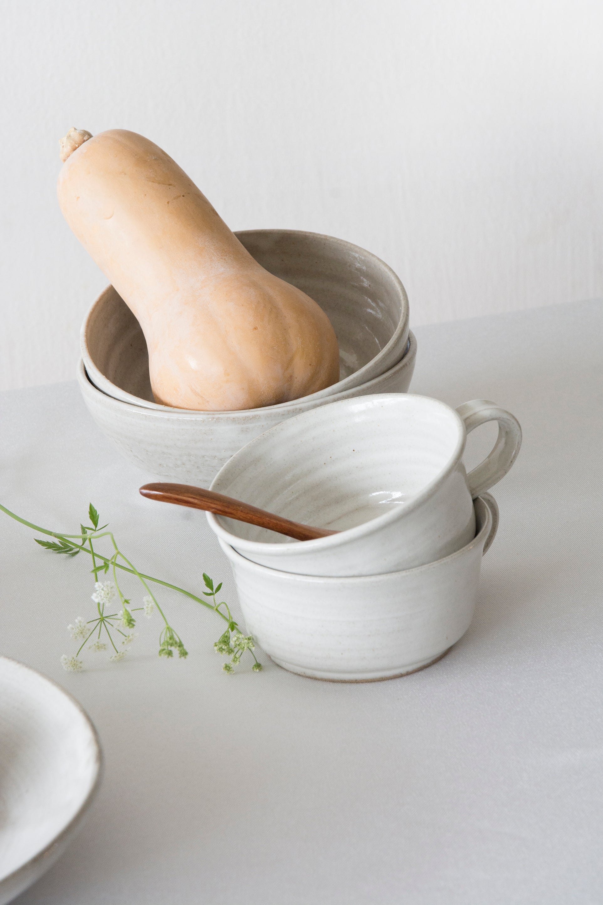 Stacked ceramic bowls with a butternut squash and wooden spoon on a light background