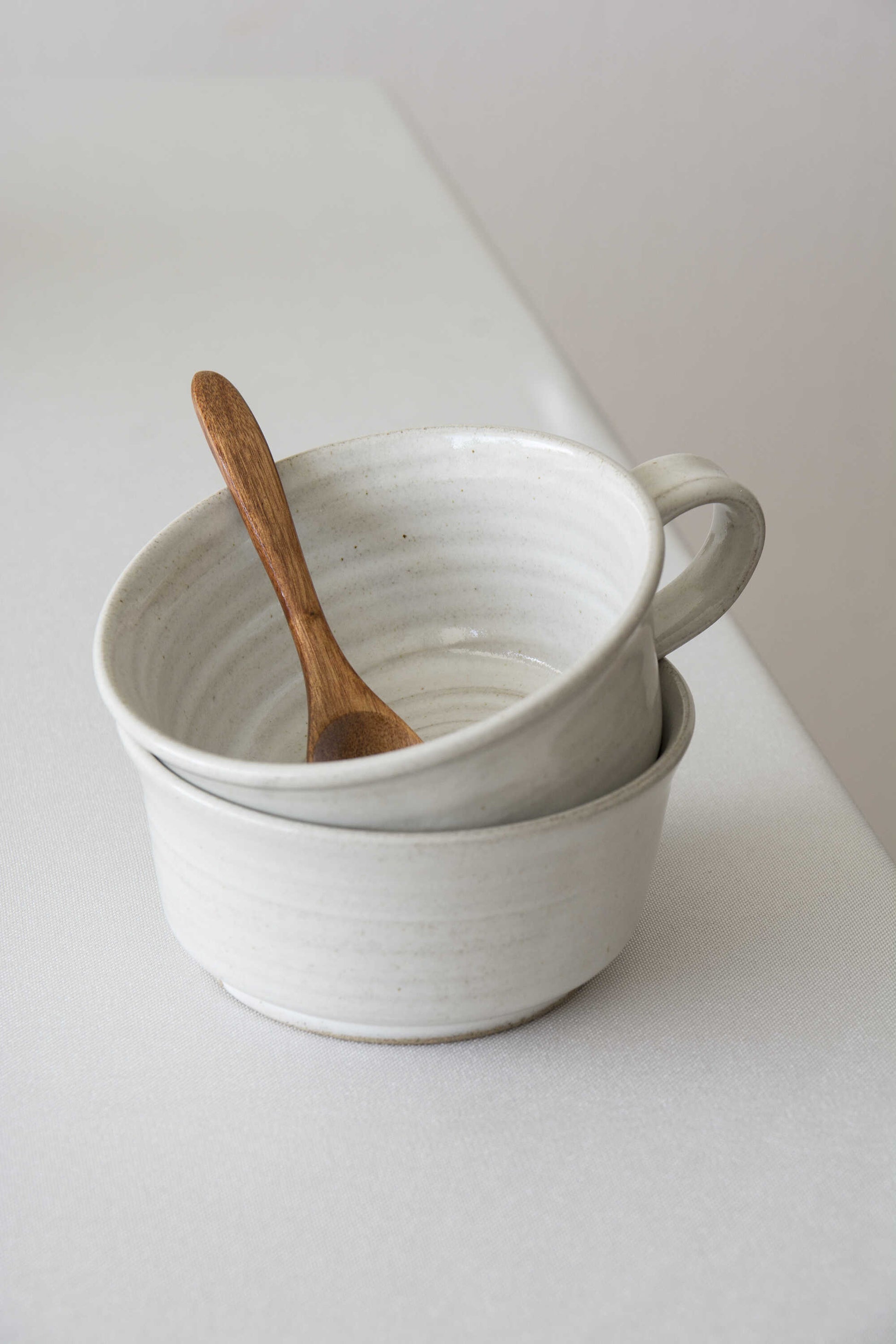 Two stacked ceramic bowls with a wooden spoon on a light surface.