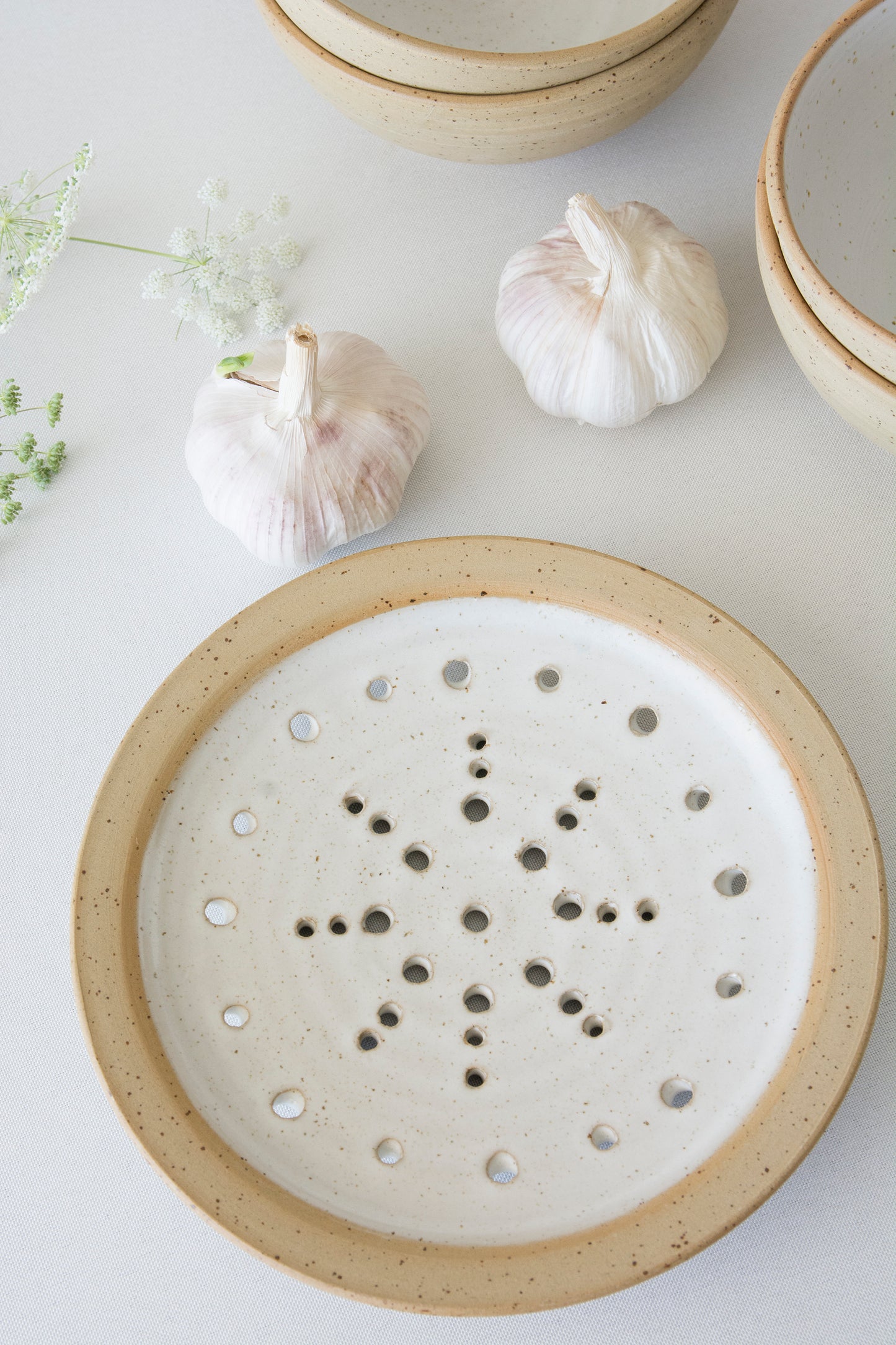 Ceramic rustic pottery plate with holes  with garlic and herbs on a light surface