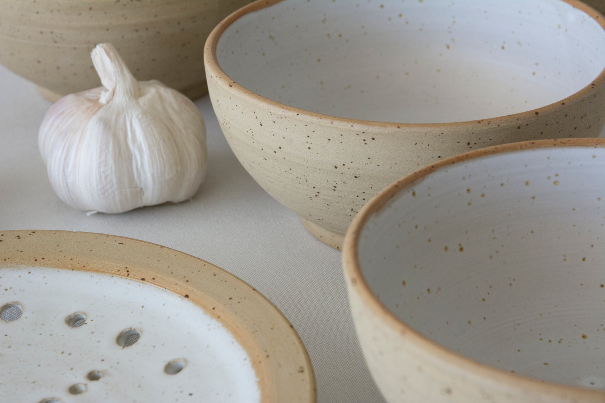 Speckled ceramic bowls on a light surface with a bulb of garlic.