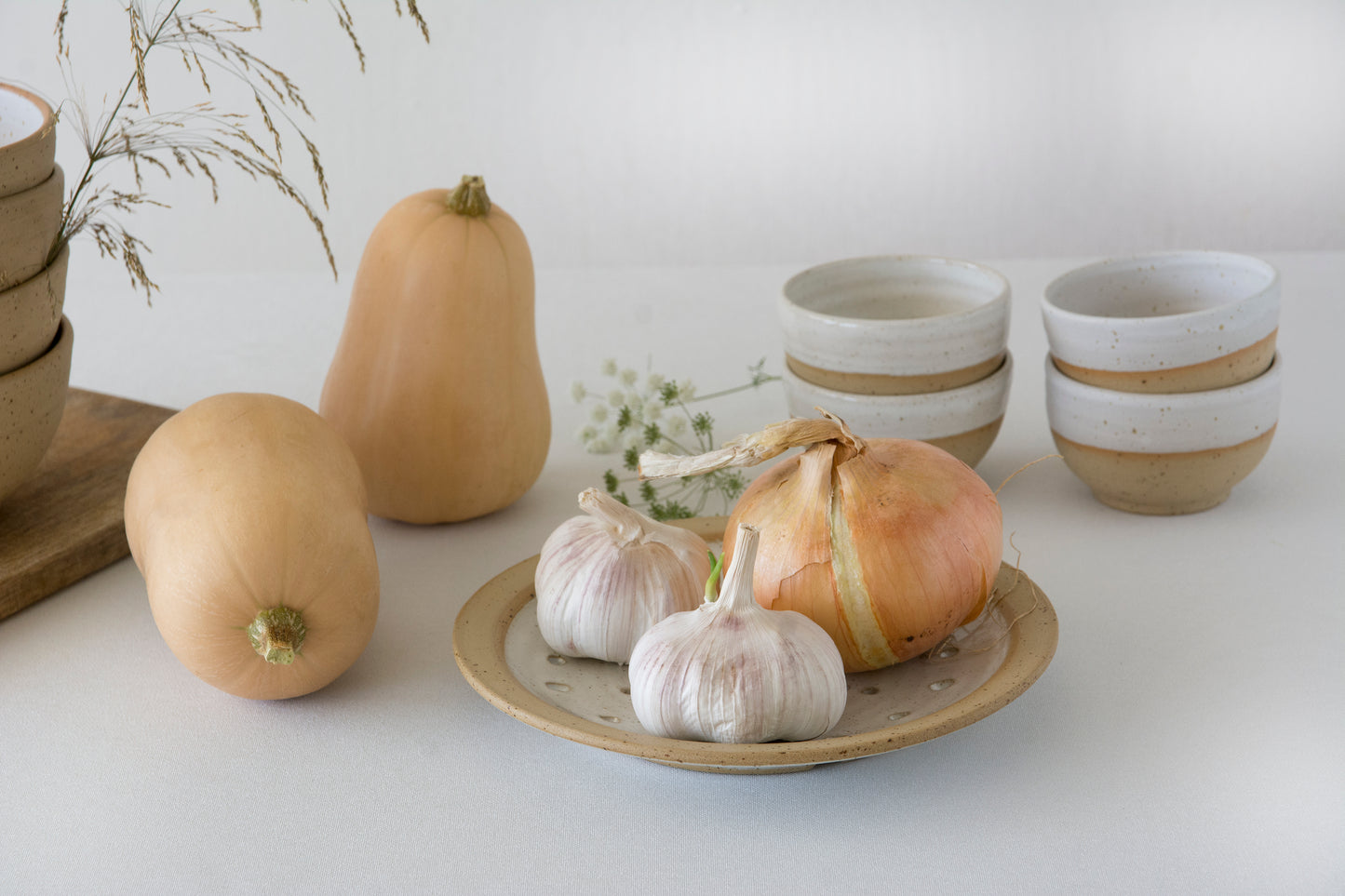 Ceramic handmade colander pottery plate and vegetables on a white surface with a neutral background