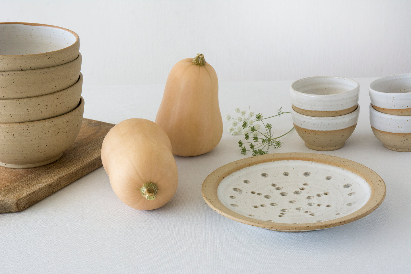 Ceramic bowls, plates, and a butternut squash on a white surface