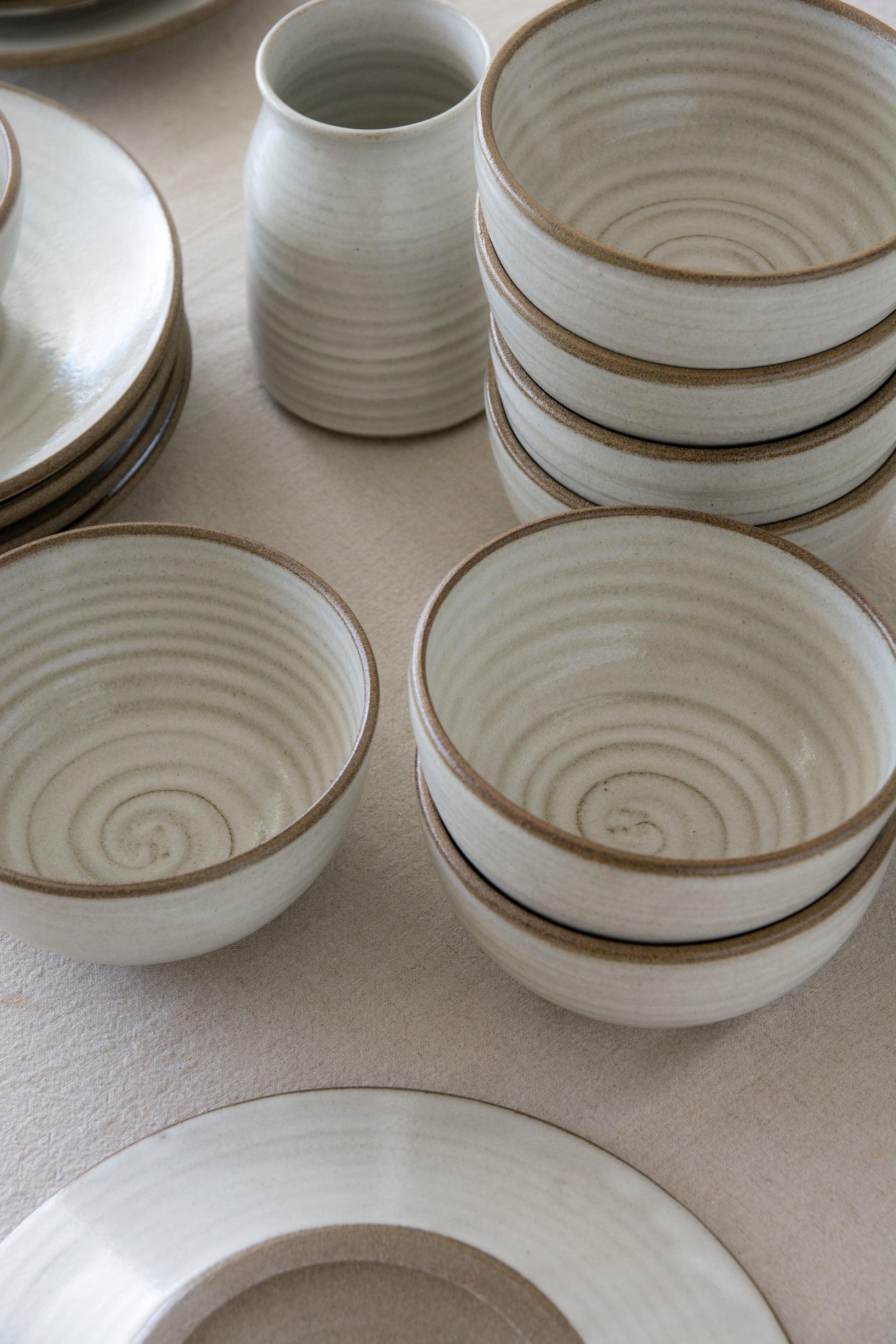 Handcrafted pottery bowl with soft white finish, stacked with matching bowls and plates