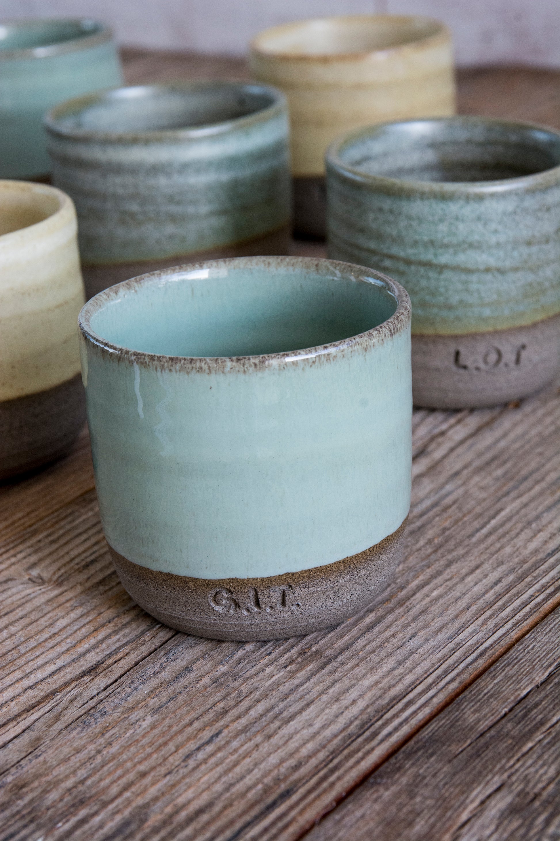 Set of ceramic cups with 'L.O.T.' branding on a wooden surface