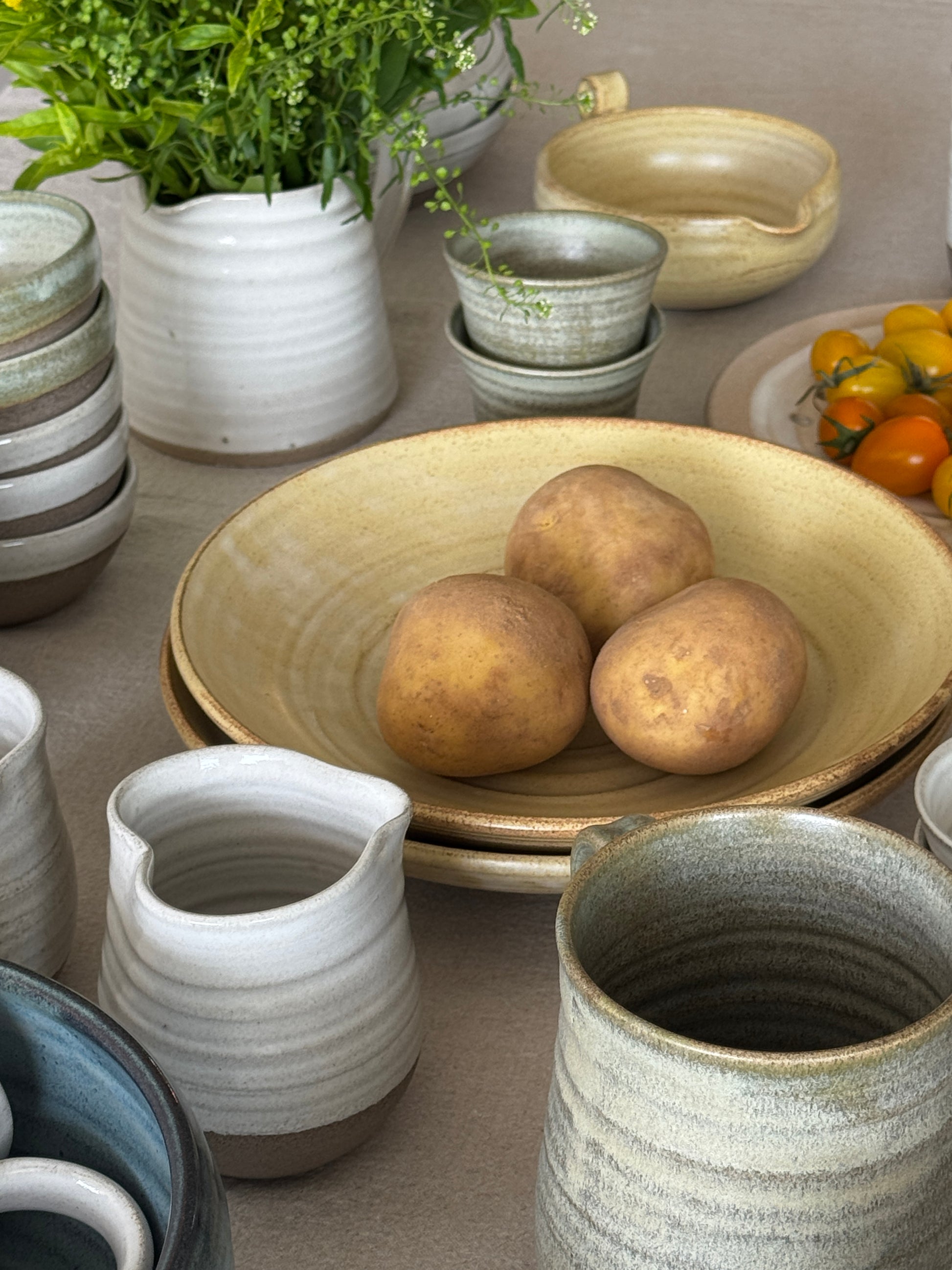Arrangement of ceramic pots with a bowl containing potatoes on a neutral background