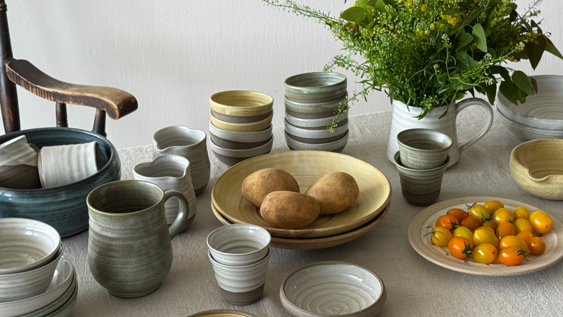 Collection of ceramic handmade dishes and bowls on a table with a plant and fruit.