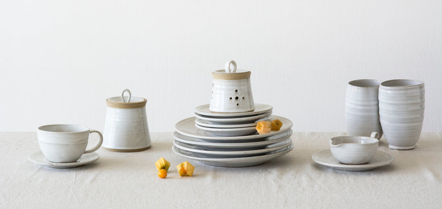 Set of ceramic dishes including plates, cups, and a teapot on a white surface with a white background.